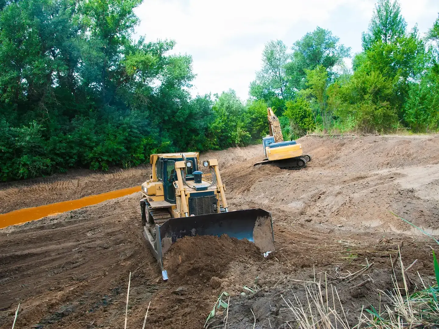 A bulldozer grading a cleared lot with the tree line behind it