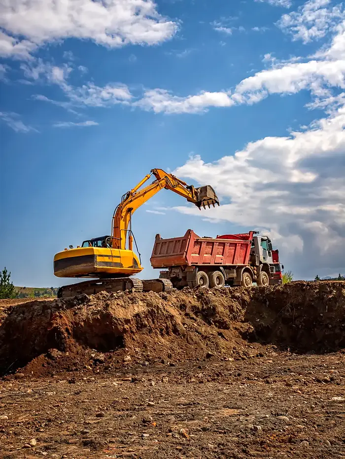 A yellow excavator loading a red dump truck
